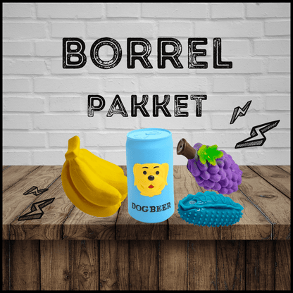 Borrelpakket met hondenspeelgoed: een gele banaan, blauwe dog beer, paarse druif en blauwe auto op een houten tafel.