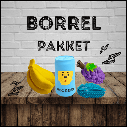 Borrelpakket met hondenspeelgoed: een gele banaan, blauwe dog beer, paarse druif en blauwe auto op een houten tafel.
